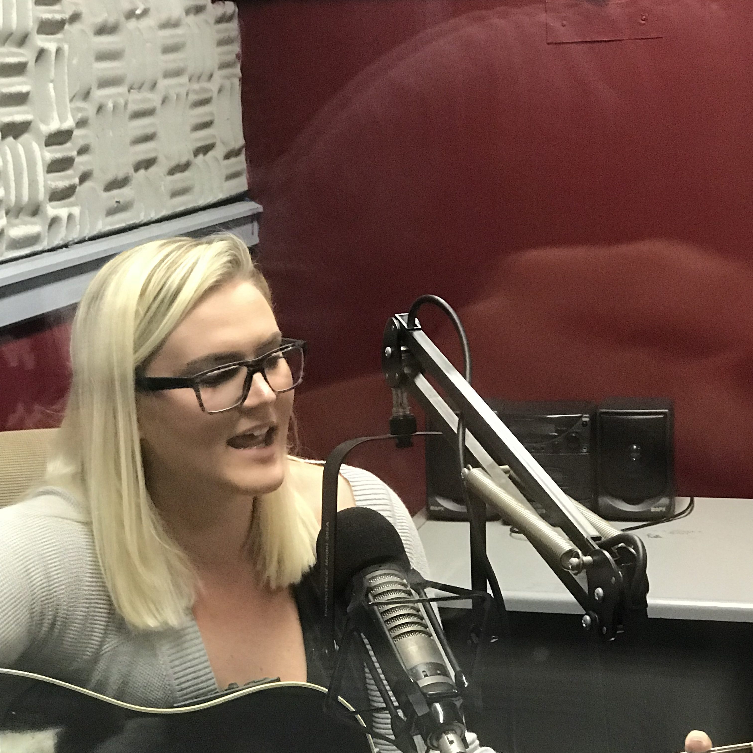 Photo of Samantha playing songs on a guitar during a radio interview.